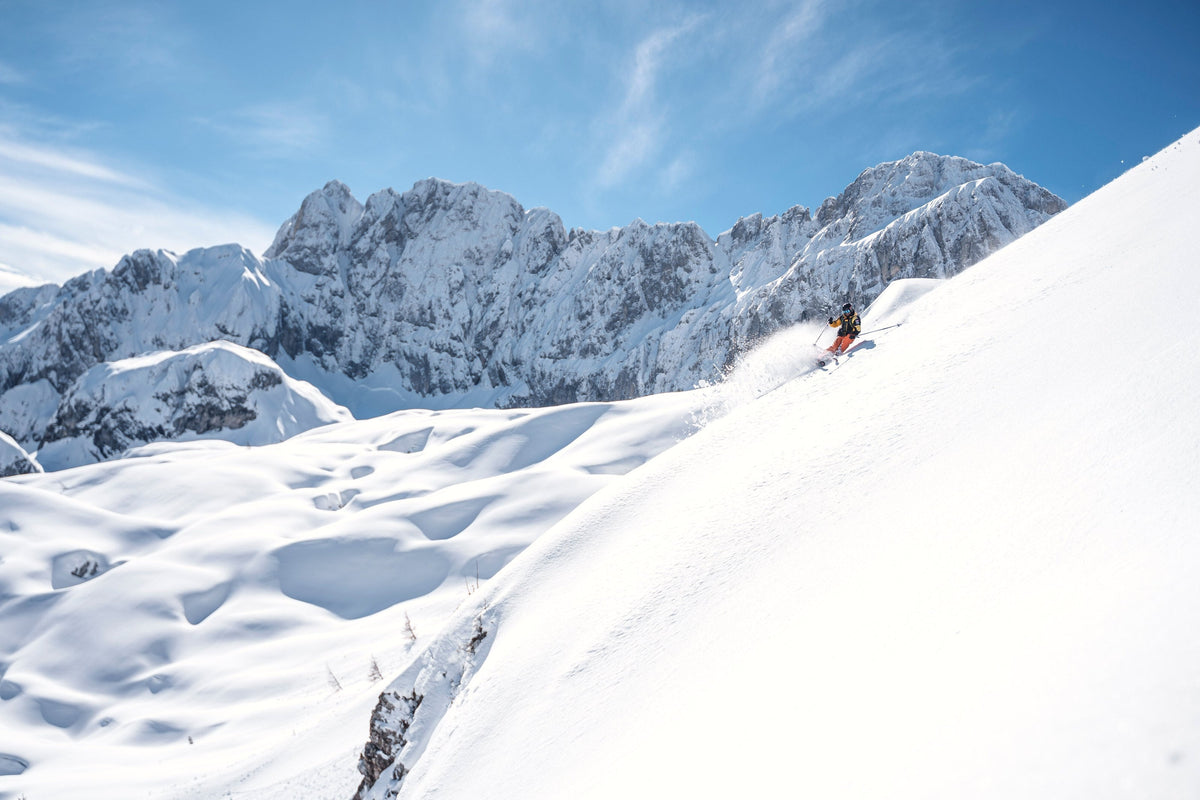 Freerider turning in powder below rocky peaks in the Italian Alps