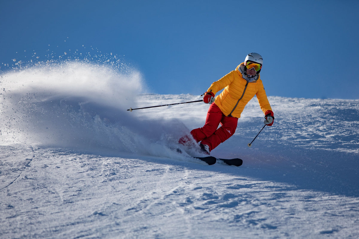 Skier in a yellow jacket carving through a spray of snow