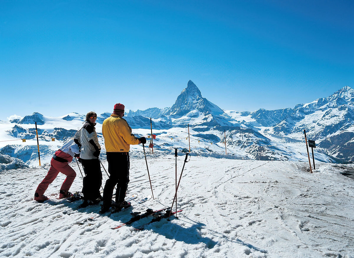 Three skiers stopping to take in the Matterhorn under a blue sky
