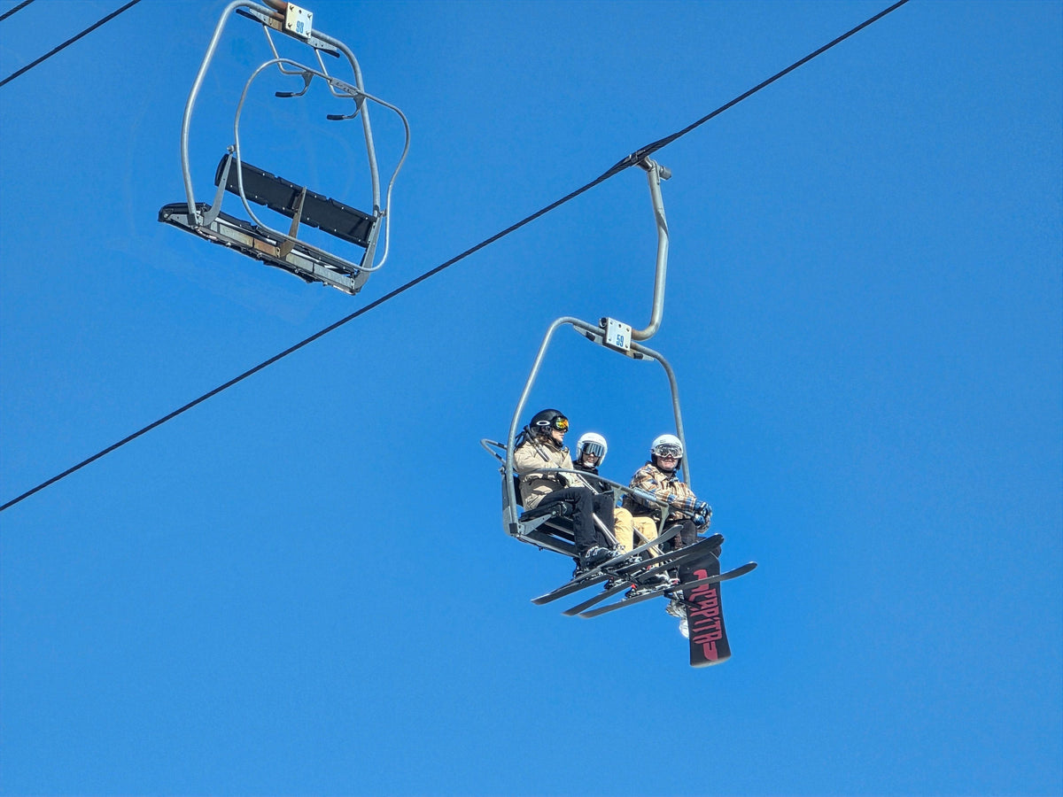 Three skiers riding a chairlift under a clear blue sky