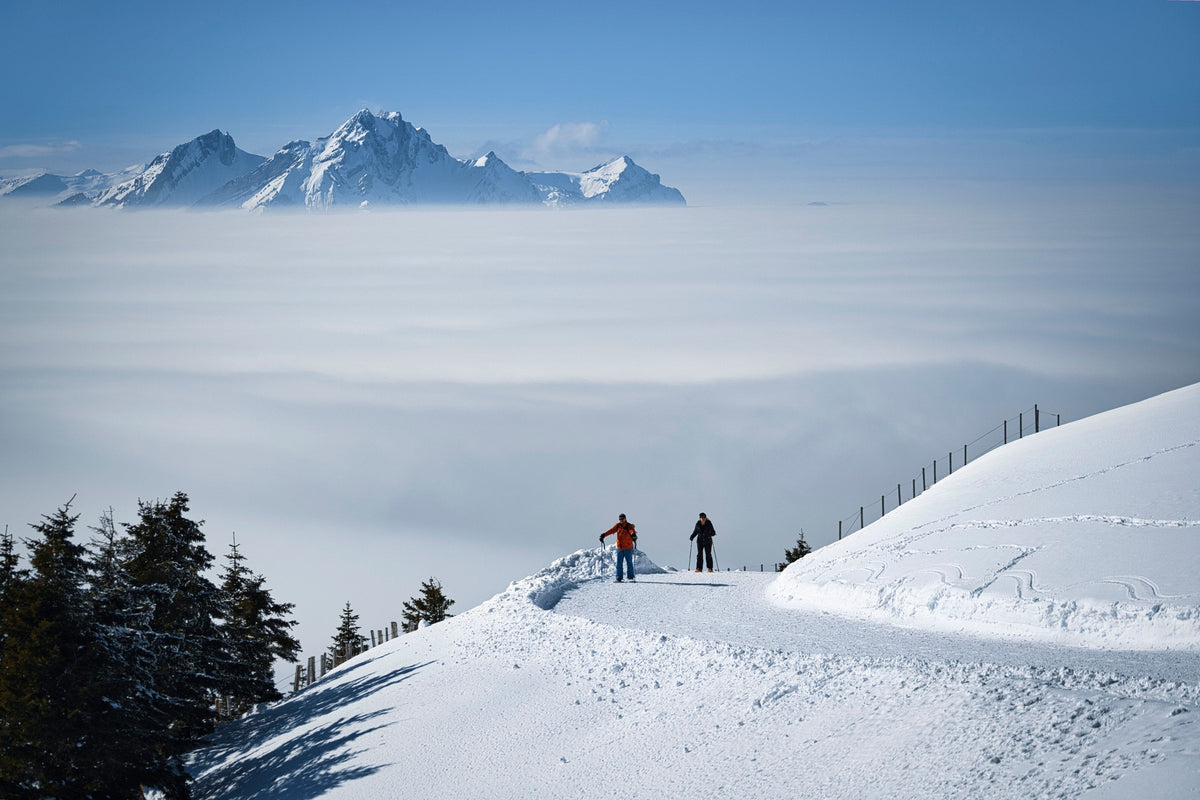Two skiers on a snowy ridge above a sea of clouds