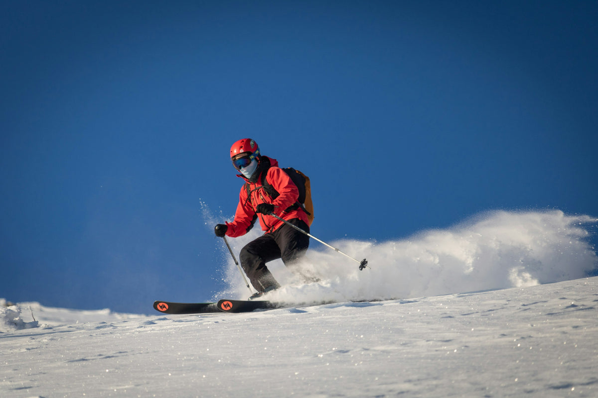 Skier in a red jacket sending up powder under a deep blue sky