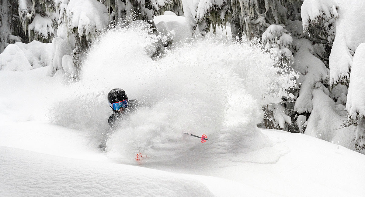 Skier in a helmet and goggles throwing a huge powder spray through snowy trees