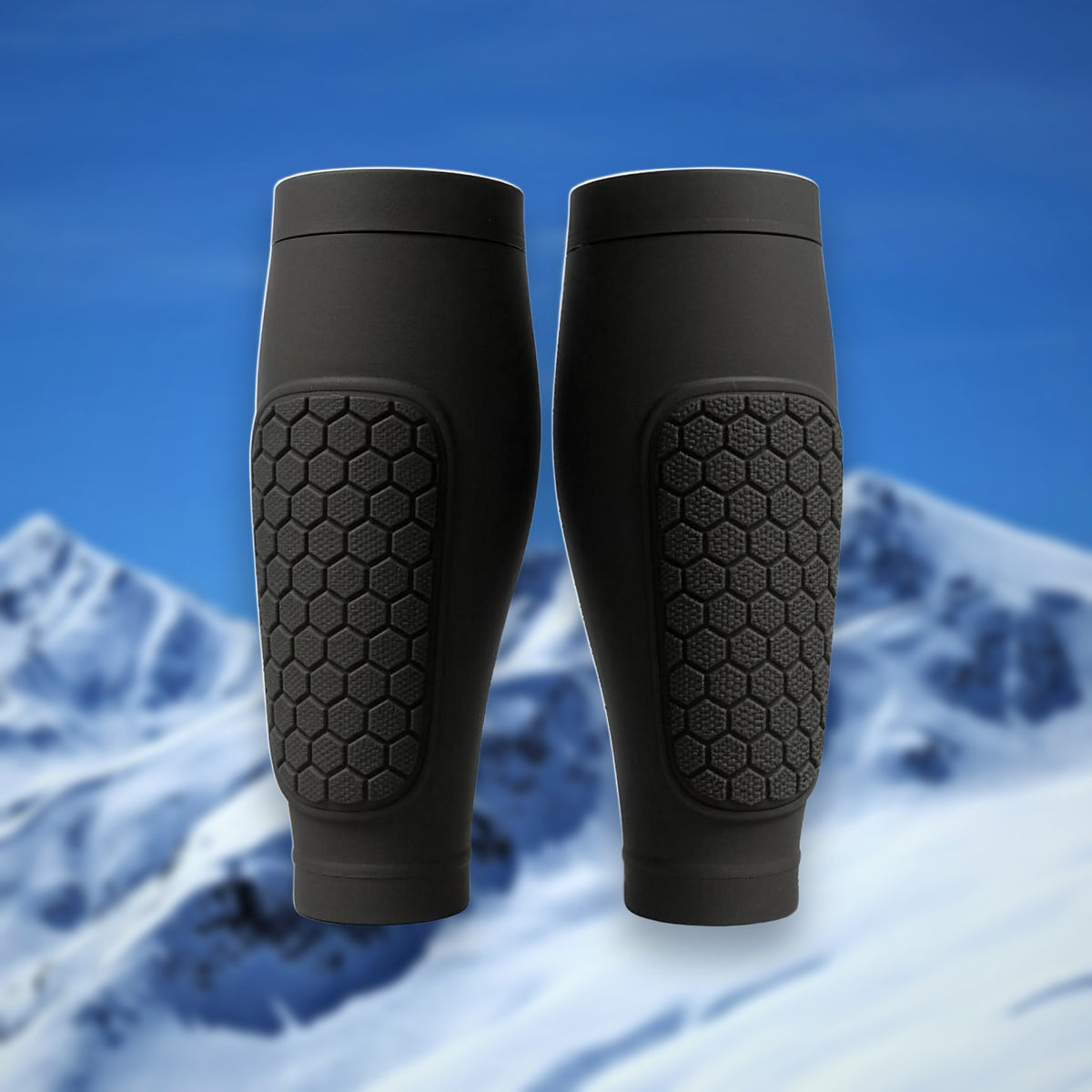Pair of Shin Bang Pads in black with honeycomb shin padding, on a snowy mountain backdrop