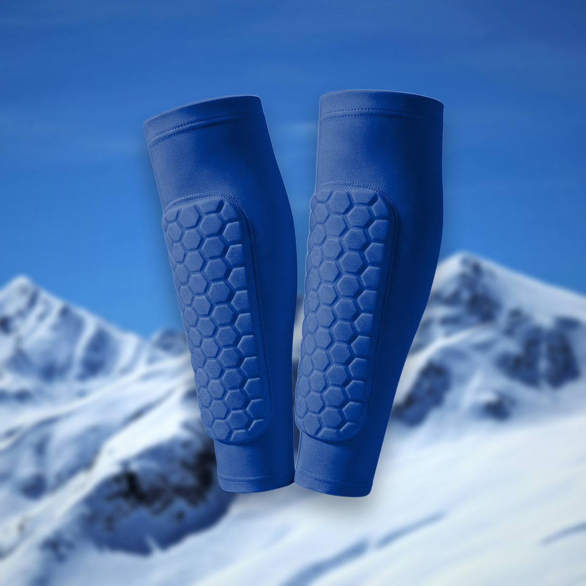 Pair of Shin Bang Pads in blue with honeycomb shin padding, on a snowy mountain backdrop