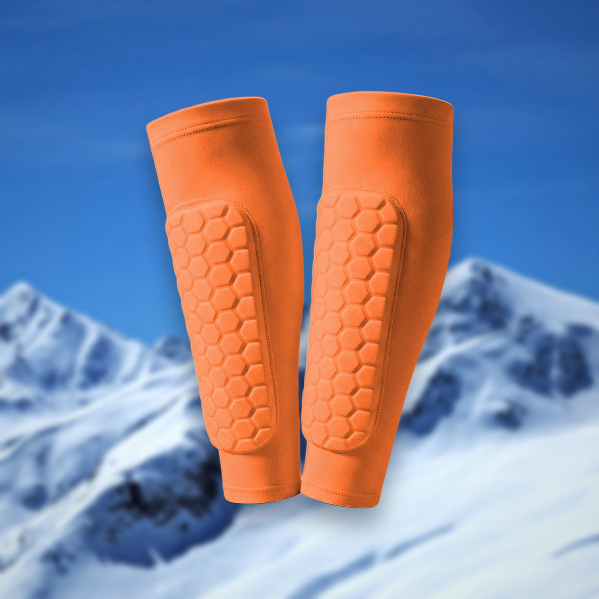 Pair of Shin Bang Pads in orange with honeycomb shin padding, on a snowy mountain backdrop
