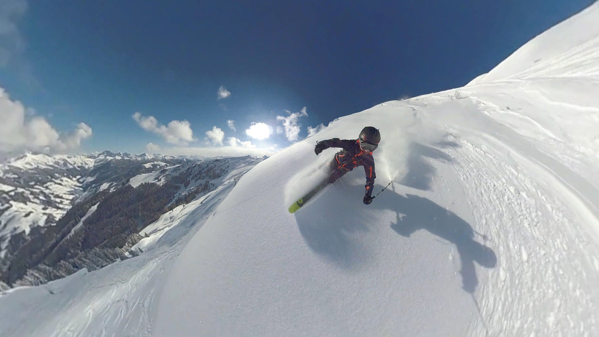Skier carving a powder turn with sunlit mountains behind