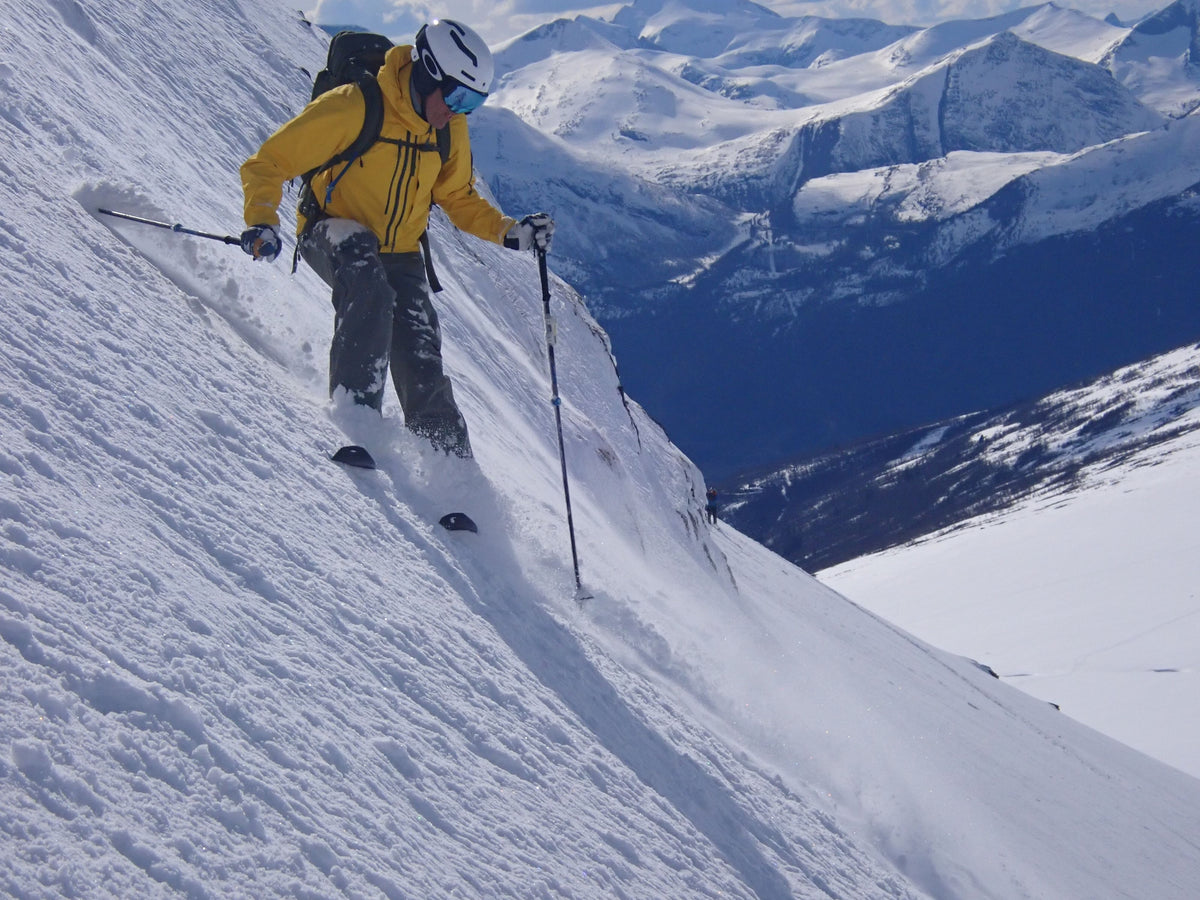 Skier descending a steep slope above a wide mountain valley