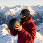 Illustrative image (AI-generated): skier looking out over the Alps wearing the Tunes Band in Black, about to put a helmet on
